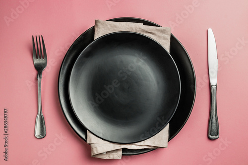 Black setting: plates, inen napkin and silverware on pink background. Top view. photo