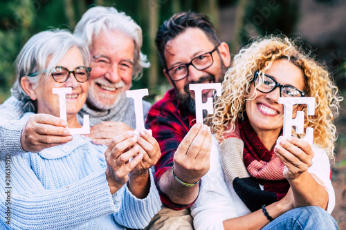 Group of mixed ages generations people smiling and showing blocks letters with  life word -  happy lifestye enjoying the outdoor leisure activity together like a family photo