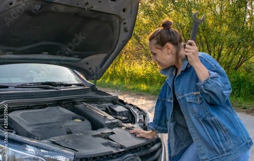 A beautiful young girl tries to change the spark plugs in the car, but does not know how to do it.