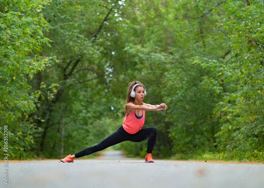 Woman stretch muscles at park before jogging. Athletic exercising outdoor.