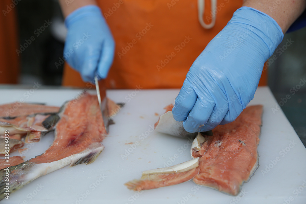 professional cutting of raw red salmon fish. Hands with a knife close-up. Fish factory, shop, production, restaurant.
