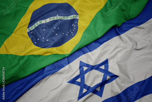 waving colorful flag of israel and national flag of brazil.