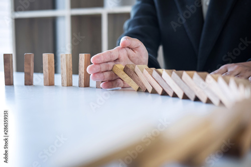 Risk and Strategy in Business, Image of hand stopping falling collapse wooden block dominoes effect from continuous toppled block, prevention and development to stability