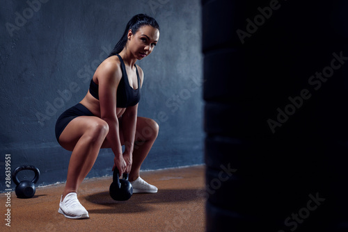 Female bodybuilder make her workout with weights - squat with kettlebell. Sexy sporty woman, with black hair.