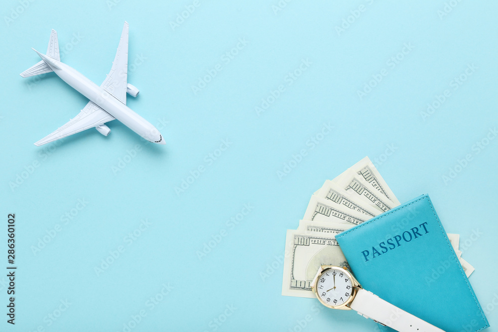 Airplane model with passport, dollar banknotes and wrist watch on blue background