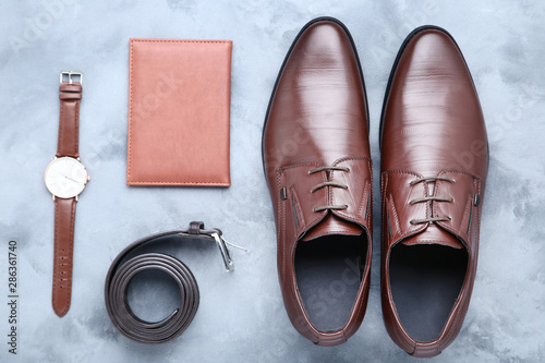 Male leather shoes with belt, passport and wrist watch on grey background