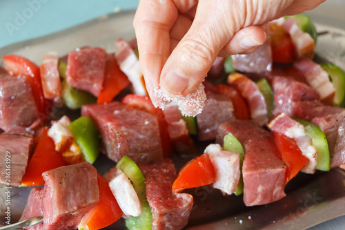 Seasoning beef brochettes on a dish with salt