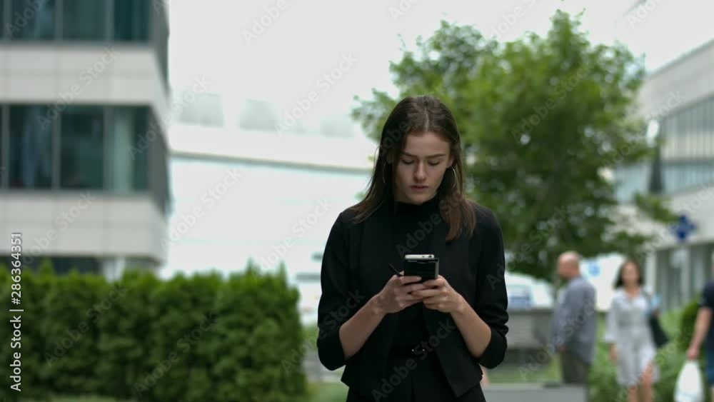 A young woman with brown hair walks towards the camera, looking intensely at her mobile phone A young woman with brown hair walks towards the camera, looking intensely at her mobile phone