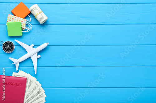 Airplane model with passport, dollar banknotes, compass and paper shopping bags on blue wooden table