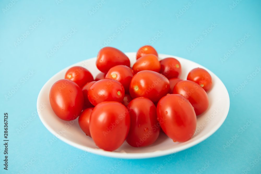 red tomatoes in white plate on blue background red tomatoes in white plate on blue background