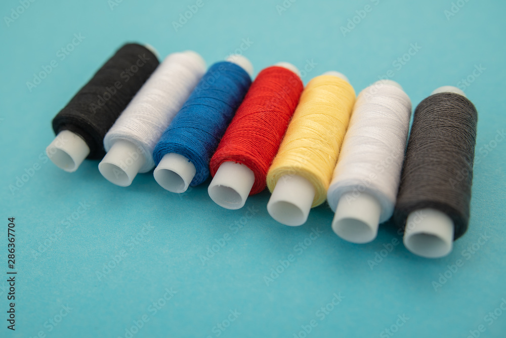 Set of sewing threads beautiful color (blue,yellow, green, white, black) on blue background Set of sewing threads beautiful color (blue,yellow, green, white, black) on blue background