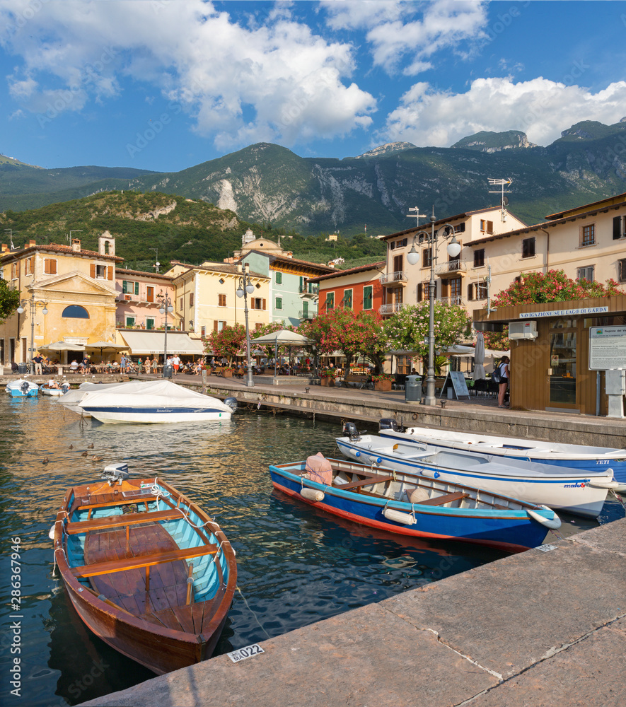 MALCESINE, ITALY - JUNE 13, 2019: The little harbor on the waterfront of Lago di Garda lake with the 2000 m high mountains in the background.