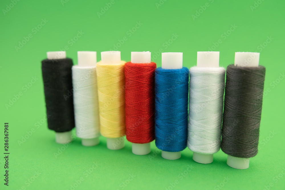 Set of sewing threads beautiful color (blue,yellow, green, white, black) on green background with space for text Set of sewing threads beautiful color (blue,yellow, green, white, black) on green background with space for text
