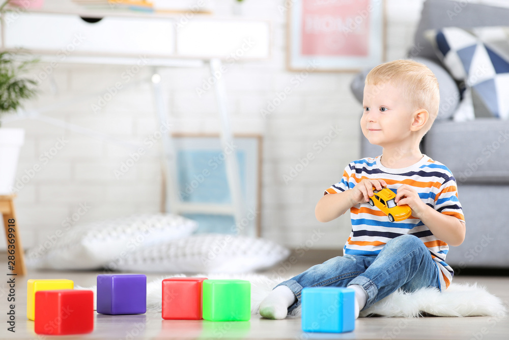 Little boy sitting on white carpet at home and playing with colorful plastic cubes and toy car Little boy sitting on white carpet at home and playing with colorful plastic cubes and toy car