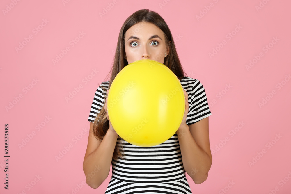 Young woman blowing yellow balloon on pink background Young woman blowing yellow balloon on pink background