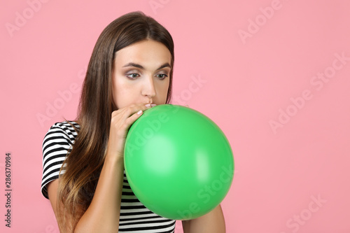 Young woman blowing green balloon on pink background © 5second