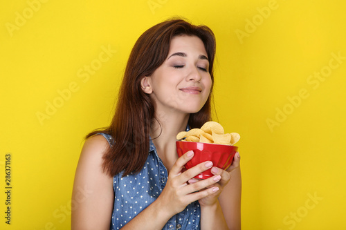 Young woman with potato chips in bowl on yellow background