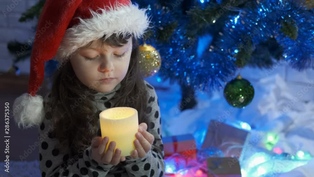 Girl and candle of holiday. Christmas child with candles. Beautiful little girl in a burning switches santaclaus hat. Girl and candle of holiday. Christmas child with candles. Beautiful little girl in a burning switches santaclaus hat.