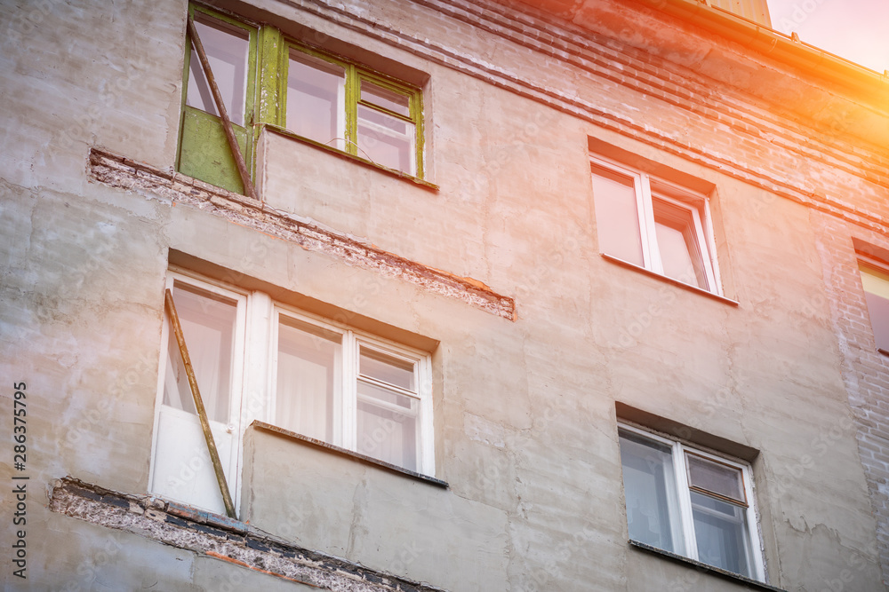 Broken concrete balcony on the facade of the building. Restoration of an old residential gray plastered house. Wooden windows and exit with door.