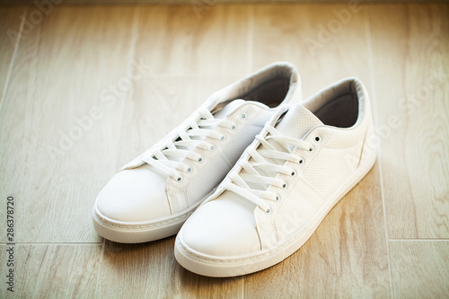 Pair of new stylish white sneakers on wood floor.