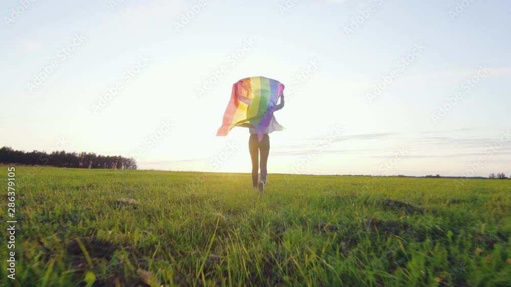Young positive woman runs across field with LGBT flag slow mo rear view Young positive woman runs across field with LGBT flag slow mo rear view