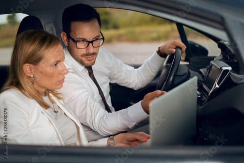 Two business colleagues using computer while going on a business travel by car