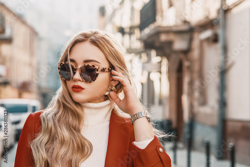 Outdoor close up street fashion portrait of young elegant woman wearing trendy autumn outfit: turtle frame sunglasses,  terracotta color blazer, white classic turtleneck. Copy, empty space for text