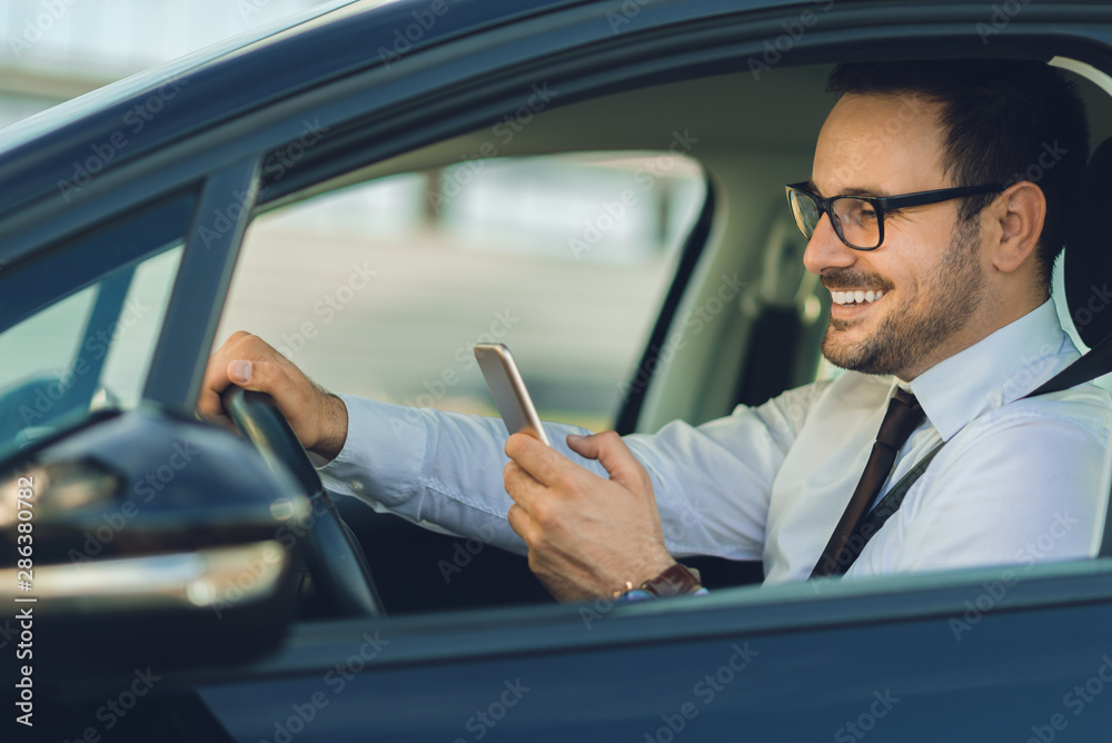 Smiling businessman using smart phone while driving a car Smiling businessman using smart phone while driving a car