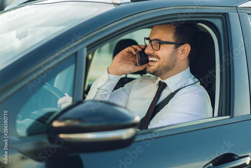 Happy businessman driving a car and talking on cell phone