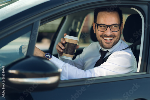 Smiling businessman driving a car while drinking coffee © Goran