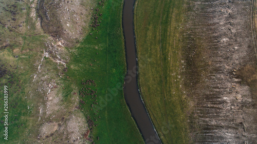 A river located in the middle of a meadow shot perpendicularly from above