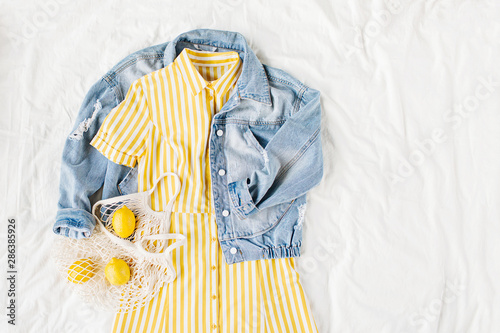 Blue jean jacket and Yellow dress  with eco bag on white bed. Women's stylish autumn or spring outfit. Trendy clothes. Fashion concept.  Flat lay, top view.