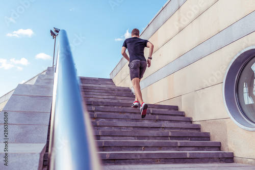A male athlete runs in the morning jogging the steps, in the summer in the city sportswear t-shirt shorts sneakers, the background of the steps handrail, free space.