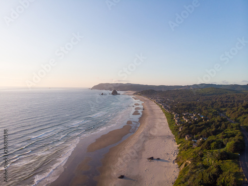 embankment of the ocean with sand and a road in the forest, at sunset shot from a high point, frame from a height