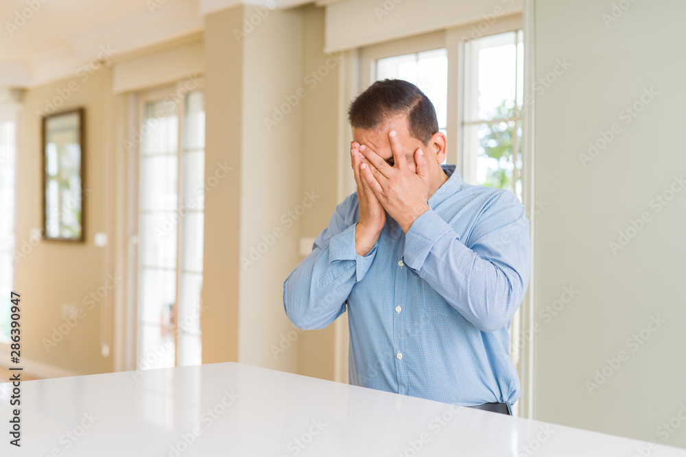 Middle age man sitting at home with sad expression covering face with hands while crying. Depression concept. Middle age man sitting at home with sad expression covering face with hands while crying. Depression concept.