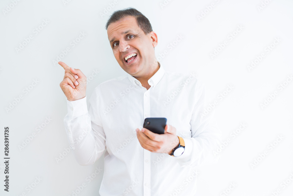 Middle age man using smartphone over white wall very happy pointing with hand and finger to the side Middle age man using smartphone over white wall very happy pointing with hand and finger to the side