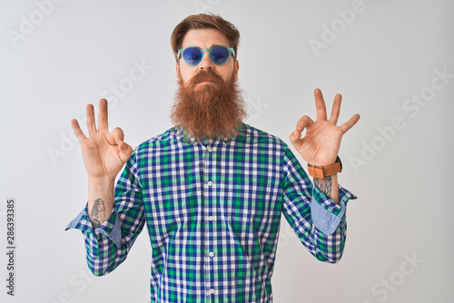 Young redhead irish man wearing casual shirt and sunglasses over isolated white background relax and smiling with eyes closed doing meditation gesture with fingers. Yoga concept.