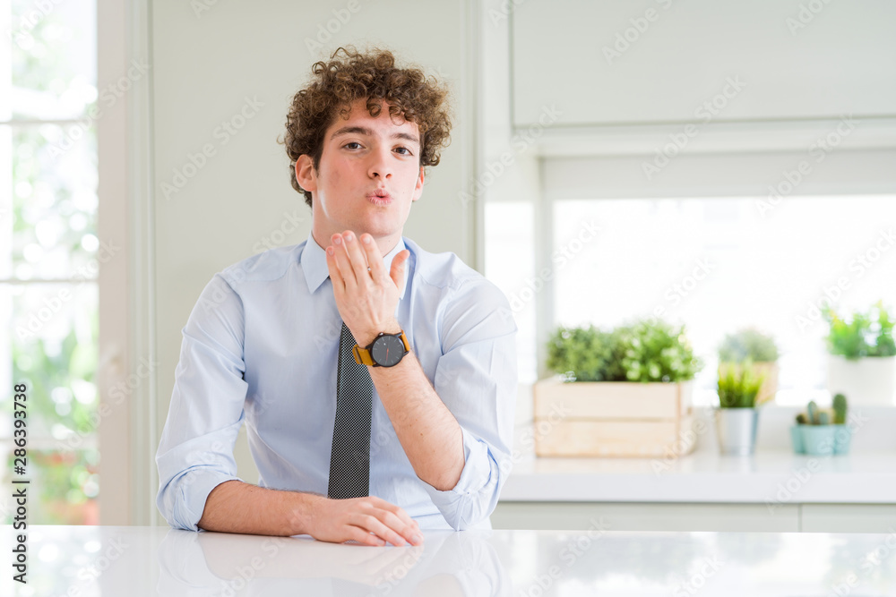 Young business man wearing a tie looking at the camera blowing a kiss with hand on air being lovely and sexy. Love expression.