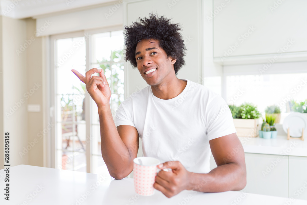 African American man with afro hair drinking a cup of coffee very happy pointing with hand and finger to the side African American man with afro hair drinking a cup of coffee very happy pointing with hand and finger to the side