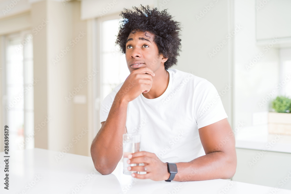 African American man drinking a glass of water at home serious face thinking about question, very confused idea African American man drinking a glass of water at home serious face thinking about question, very confused idea