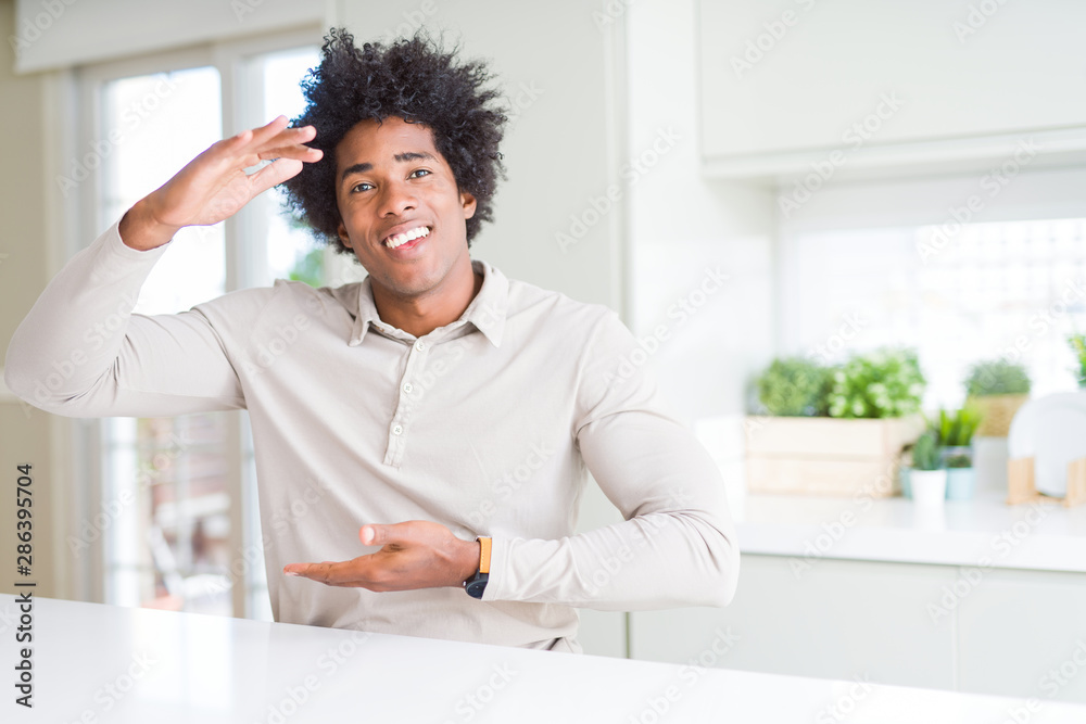 African American man at home gesturing with hands showing big and large size sign, measure symbol. Smiling looking at the camera. Measuring concept.