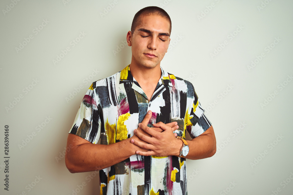 Young handsome man wearing summer shirt over white isolated background smiling with hands on chest with closed eyes and grateful gesture on face. Health concept. Young handsome man wearing summer shirt over white isolated background smiling with hands on chest with closed eyes and grateful gesture on face. Health concept.