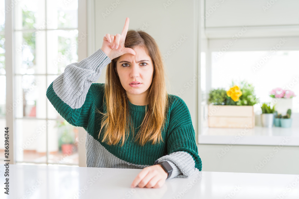 Young beautiful plus size woman wearing casual striped sweater making fun of people with fingers on forehead doing loser gesture mocking and insulting.