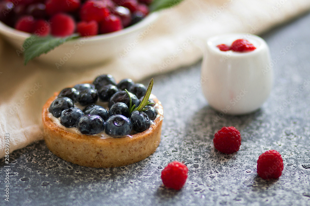 Tartalette with blueberry berries, plate with fresh raspberry and dairy with sour cream on the grey surface. 