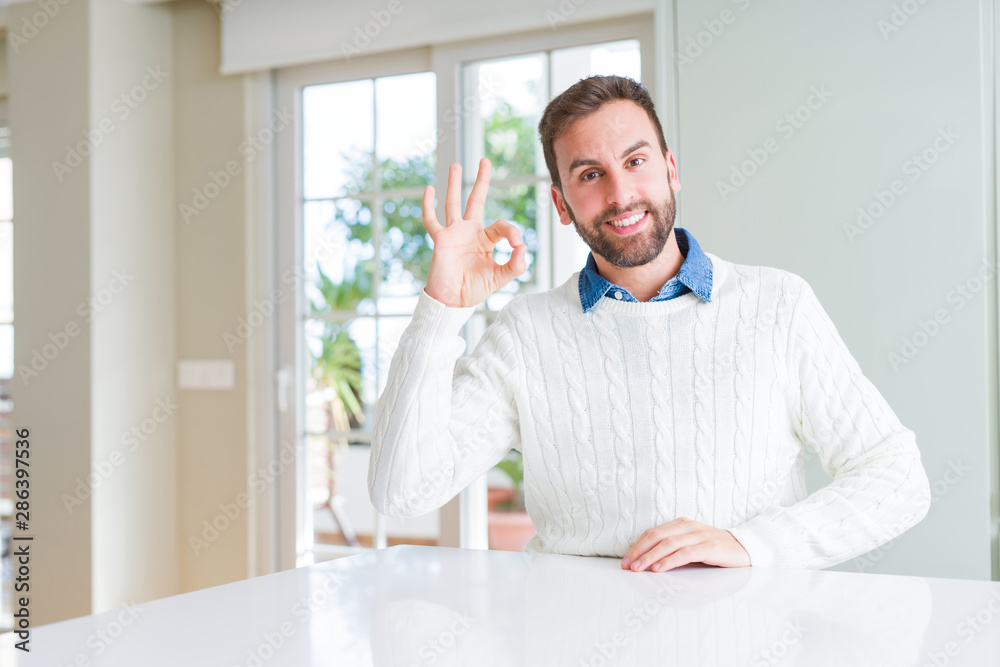 Handsome man wearing casual sweater smiling positive doing ok sign with hand and fingers. Successful expression.