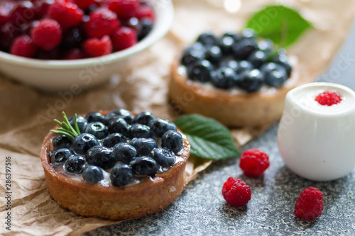Tartalets with blueberry berries, plate with fresh raspberry and dairy with sour cream on the grey surface. 