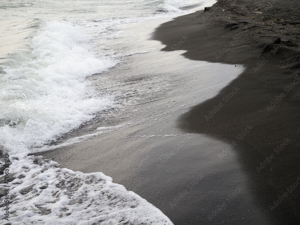 White foam wave on the black sand beach.