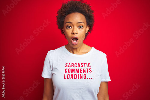 African american woman wearing sarcastic comments t-shirt over red isolated background afraid and shocked with surprise expression, fear and excited face. photo