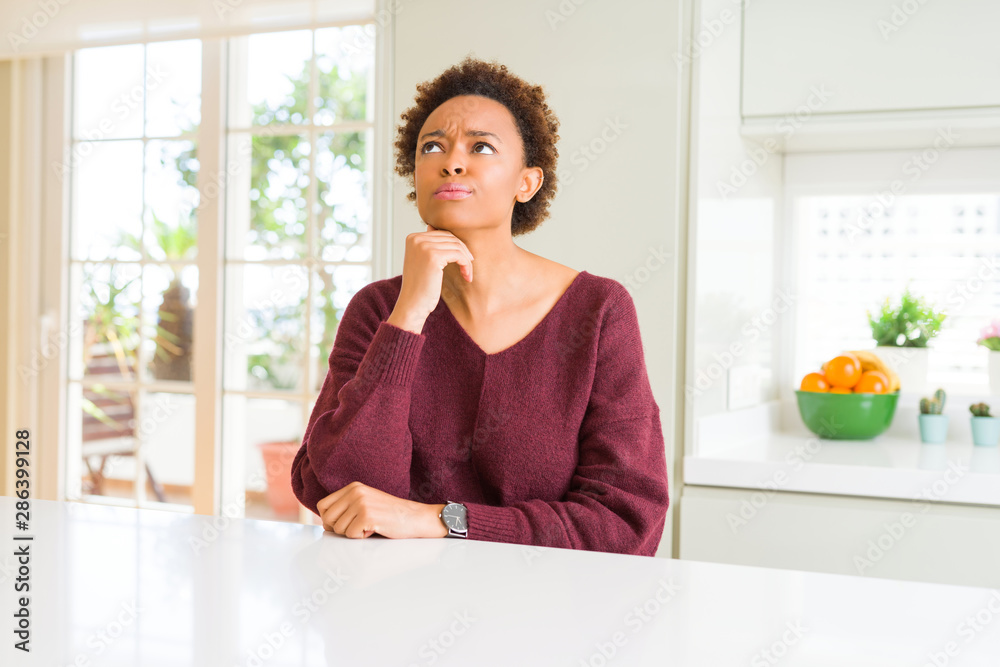 Young beautiful african american woman at home with hand on chin thinking about question, pensive expression. Smiling with thoughtful face. Doubt concept.