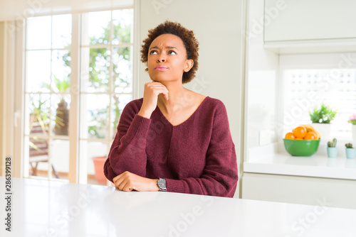 Young beautiful african american woman at home with hand on chin thinking about question  pensive expression. Smiling with thoughtful face. Doubt concept.